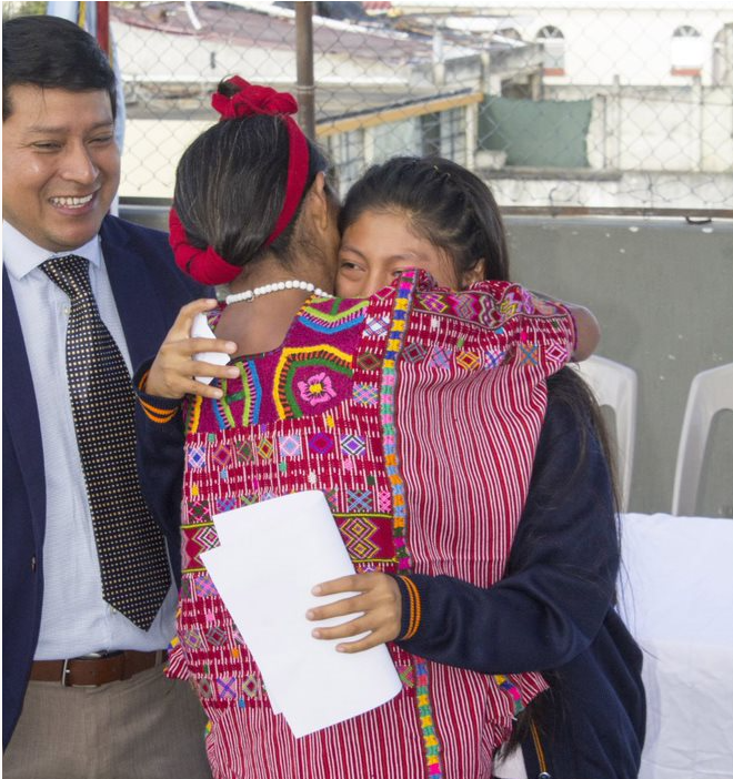 team-member-spotlight-lucas-pinzon scholar hugs her mom at ceremony as Lucas Pinzon smiles on approvingly